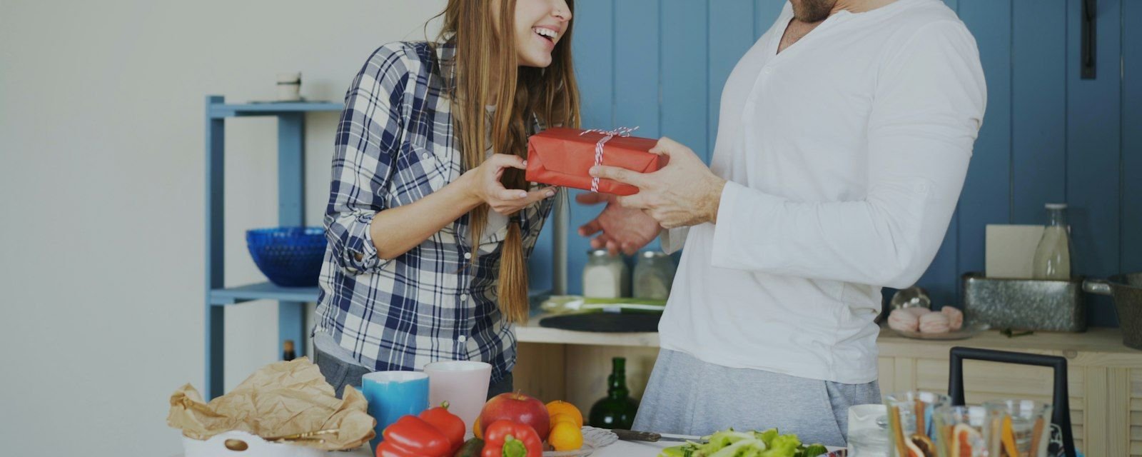 Two people exchanging a wrapped gift in a home kitchen