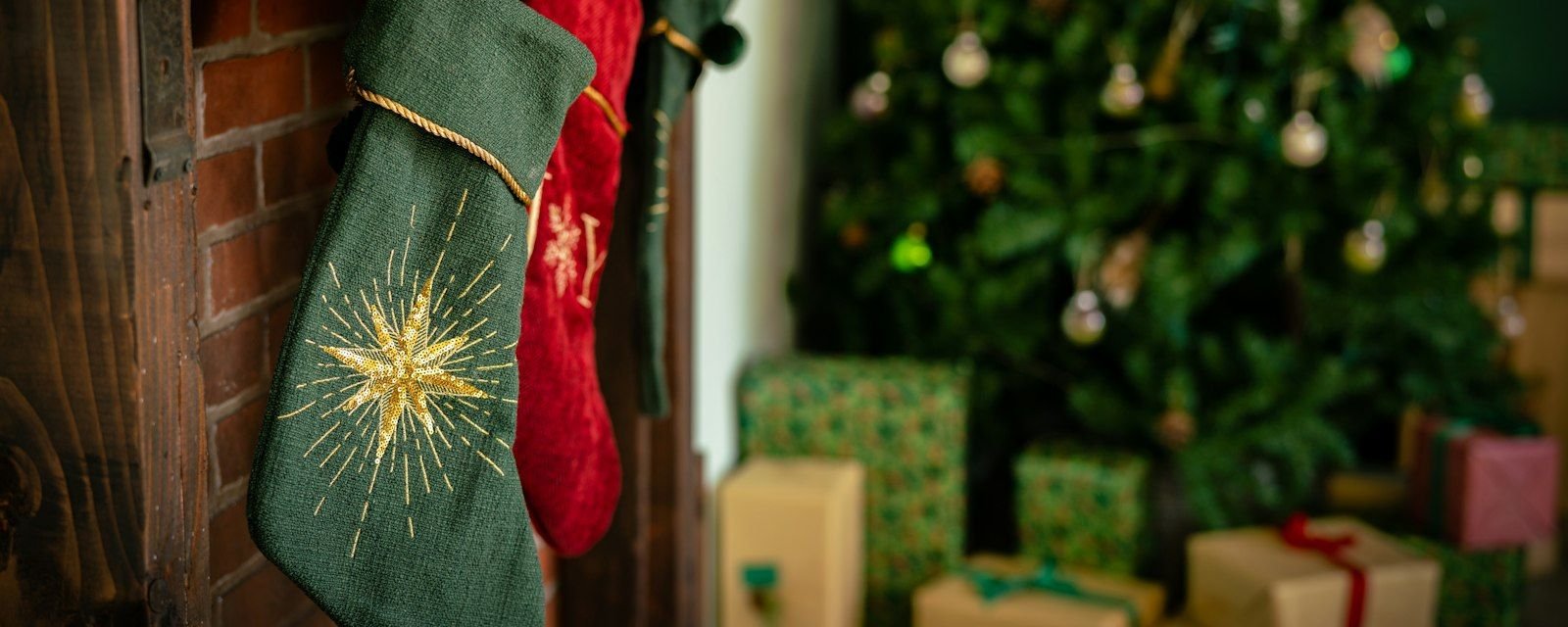 A Christmas stocking hanging by a decorated tree with wrapped presents